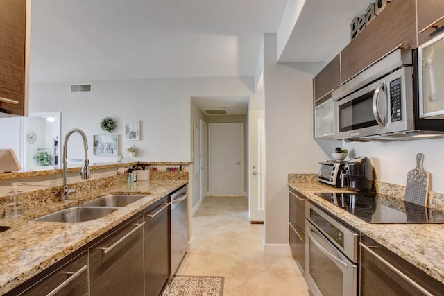 kitchen featuring light tile patterned floors, sink, light stone counters, stainless steel appliances, and dark brown cabinetry