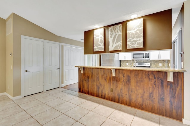 kitchen featuring stainless steel refrigerator, light tile patterned flooring, kitchen peninsula, vaulted ceiling, and white cabinets