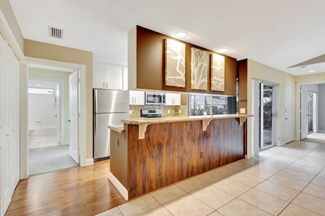 kitchen featuring kitchen peninsula, decorative backsplash, stainless steel appliances, light tile patterned floors, and white cabinetry