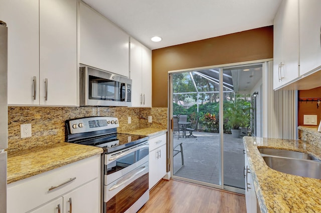 kitchen featuring light stone countertops, stainless steel appliances, tasteful backsplash, light hardwood / wood-style flooring, and white cabinets