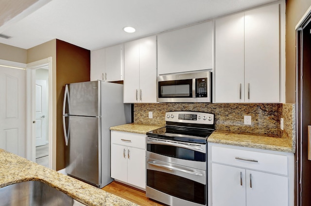 kitchen with backsplash, white cabinets, light wood-type flooring, light stone counters, and stainless steel appliances