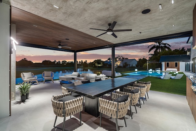 patio terrace at dusk with a water view, a swimming pool, and ceiling fan