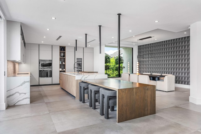 kitchen featuring sink, stainless steel double oven, a kitchen breakfast bar, and a large island with sink