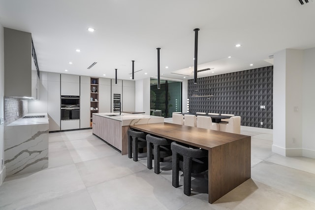 kitchen featuring tasteful backsplash, pendant lighting, sink, double oven, and a kitchen island with sink