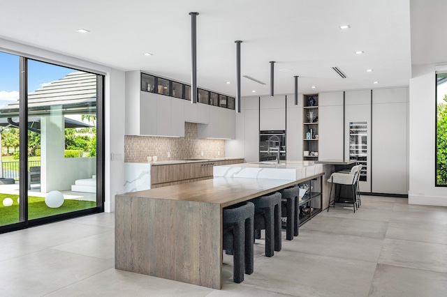 kitchen with tasteful backsplash, sink, a kitchen island with sink, light tile patterned flooring, and white cabinetry