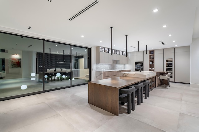 kitchen with a breakfast bar, pendant lighting, backsplash, oven, and a large island