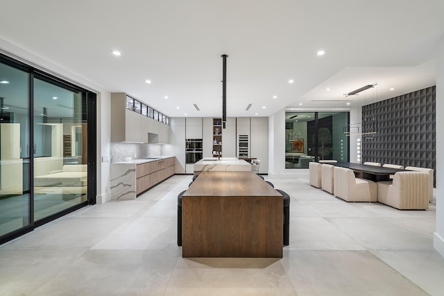 kitchen with light tile patterned floors, a kitchen island, black double oven, hanging light fixtures, and decorative backsplash