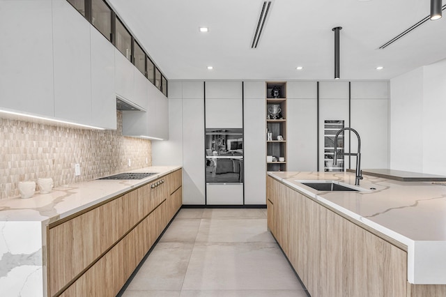 kitchen with white cabinetry, tasteful backsplash, light stone counters, gas cooktop, and sink