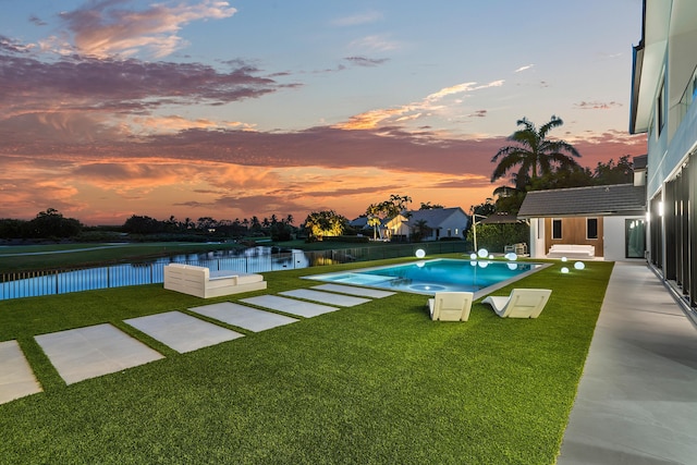 pool at dusk featuring a water view, an outbuilding, and a lawn