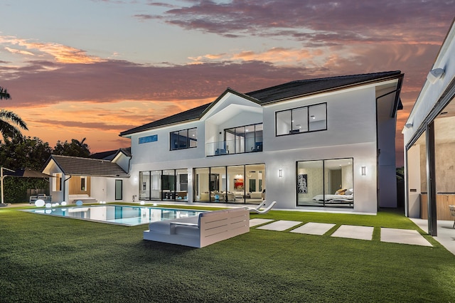 back house at dusk featuring a balcony, a yard, and a patio area