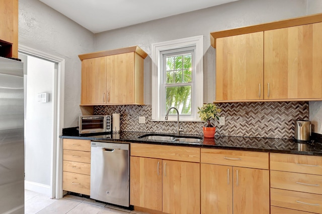 kitchen with decorative backsplash, light tile patterned floors, stainless steel appliances, light brown cabinetry, and dark stone counters