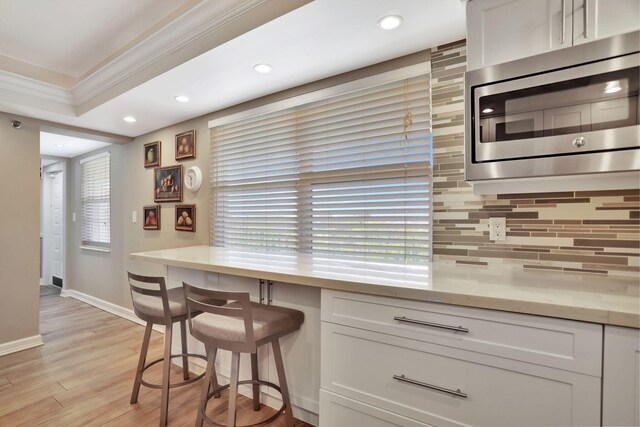 kitchen featuring stainless steel microwave, crown molding, light hardwood / wood-style flooring, tasteful backsplash, and white cabinets