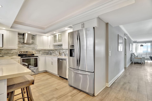 kitchen with white cabinetry, tasteful backsplash, wall chimney range hood, light hardwood / wood-style floors, and appliances with stainless steel finishes