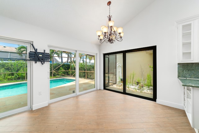 unfurnished dining area featuring a notable chandelier, light wood-type flooring, lofted ceiling, and built in features