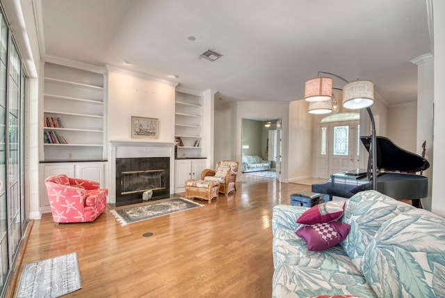 living room featuring crown molding, light wood-type flooring, built in features, a textured ceiling, and a high end fireplace