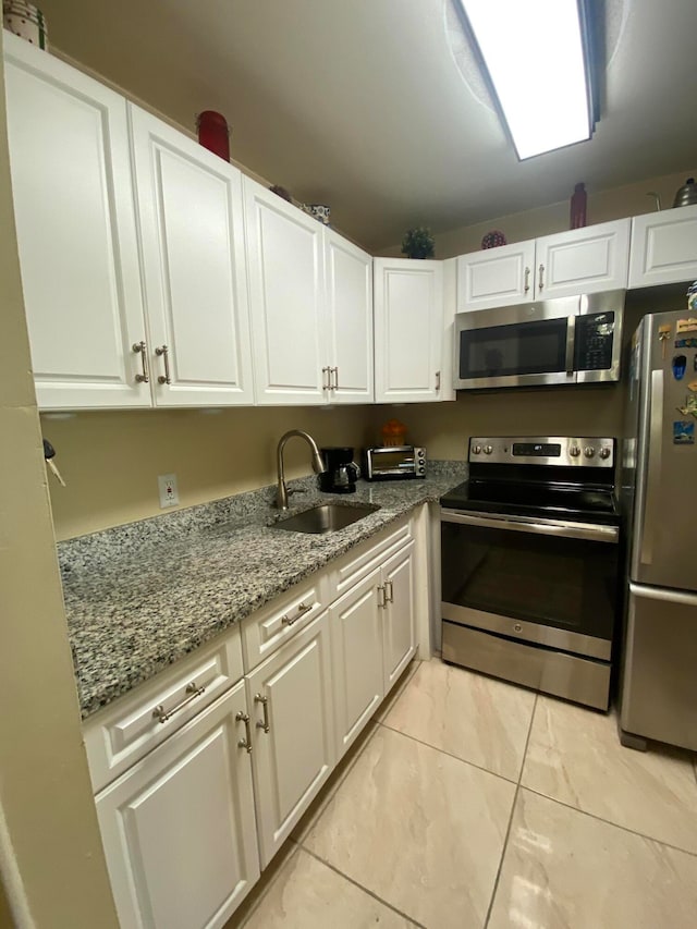 kitchen featuring light stone counters, stainless steel appliances, light tile patterned floors, sink, and white cabinets