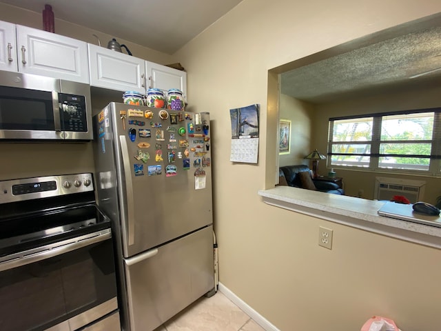 kitchen with white cabinets, a wall unit AC, light tile patterned flooring, and stainless steel appliances