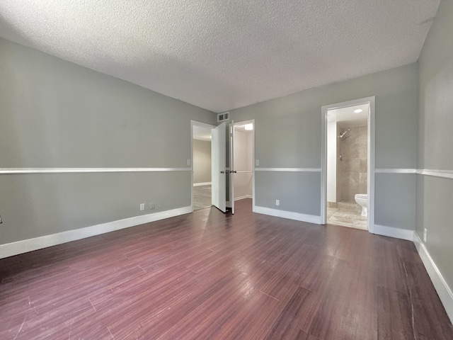 unfurnished bedroom with dark wood-style flooring, visible vents, connected bathroom, a textured ceiling, and baseboards