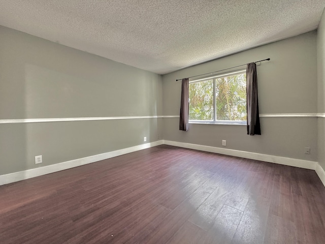 empty room with dark wood-style floors, a textured ceiling, and baseboards