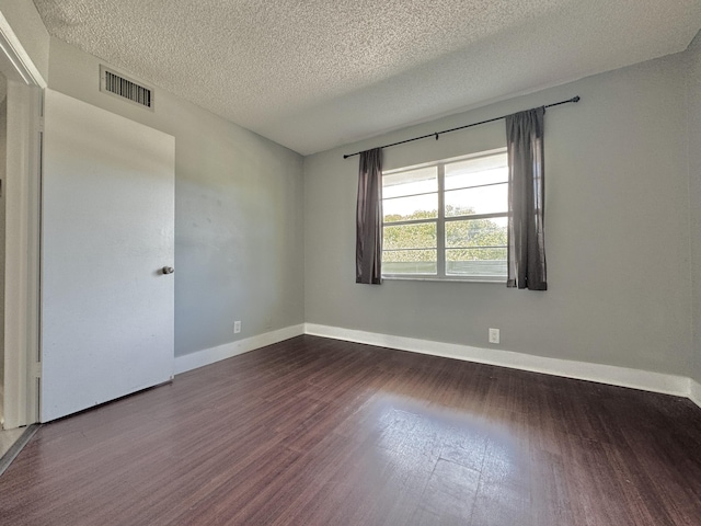 spare room featuring a textured ceiling, dark wood finished floors, visible vents, and baseboards