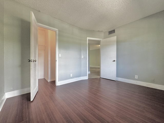 unfurnished bedroom featuring dark wood-style floors, a textured ceiling, visible vents, and baseboards