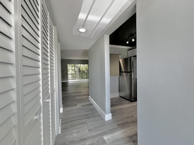 hall featuring light wood-type flooring, baseboards, and a textured wall