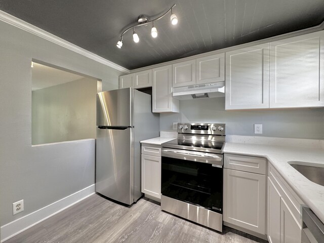 kitchen with under cabinet range hood, white cabinetry, appliances with stainless steel finishes, and crown molding