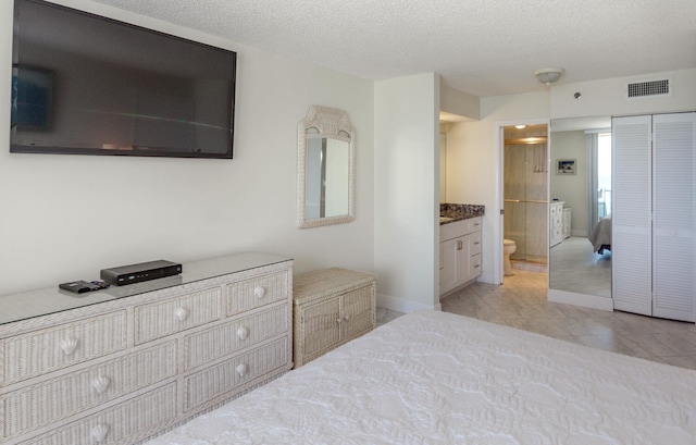 bedroom featuring a textured ceiling, connected bathroom, and light tile patterned floors