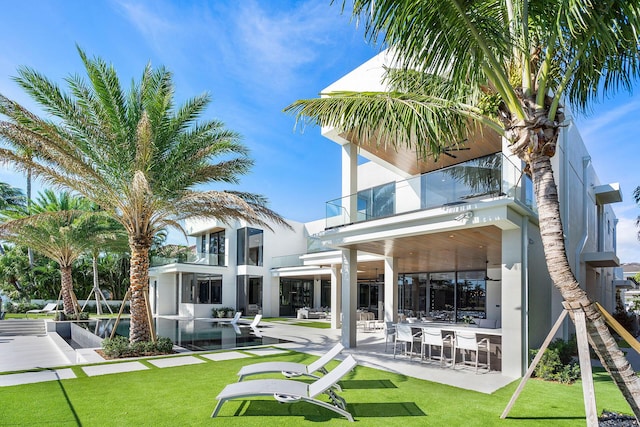 rear view of property featuring a balcony, a yard, exterior bar, and a patio