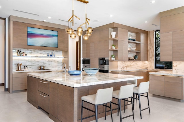 kitchen with backsplash, a large island with sink, a kitchen breakfast bar, hanging light fixtures, and light stone countertops