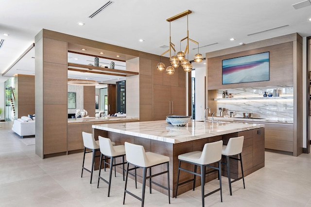 kitchen with light stone counters, a breakfast bar, hanging light fixtures, and a large island