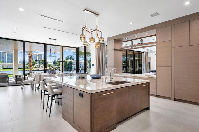 kitchen with pendant lighting, sink, a spacious island, light stone counters, and expansive windows