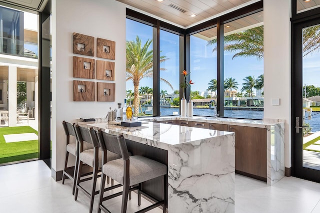 bar featuring a wall of windows, a water view, wood ceiling, and light stone counters