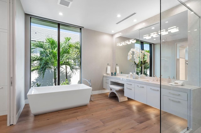 bathroom featuring a wall of windows, hardwood / wood-style floors, plenty of natural light, vanity, and a tub