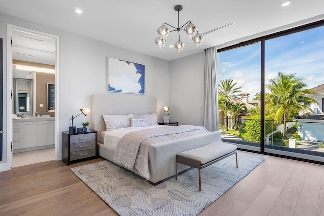 bedroom with sink, ensuite bath, a chandelier, light wood-type flooring, and a wall of windows