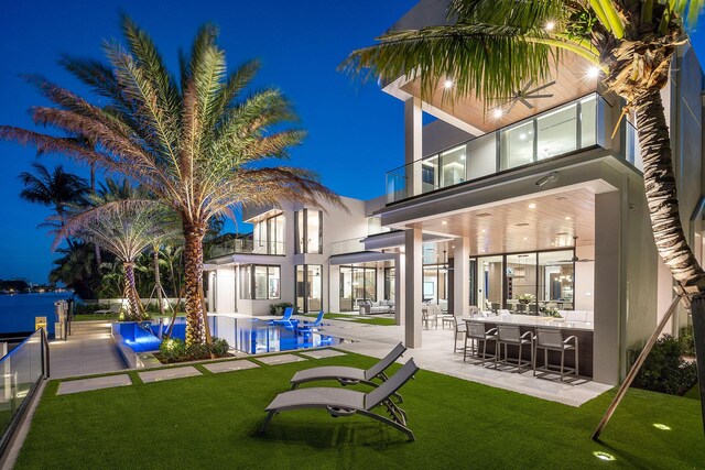 back house at twilight with a balcony, a yard, an outdoor bar, and a patio