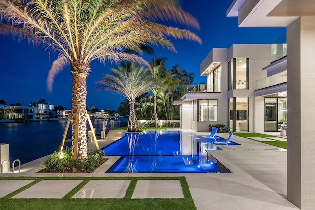 pool at twilight with a water view and a patio