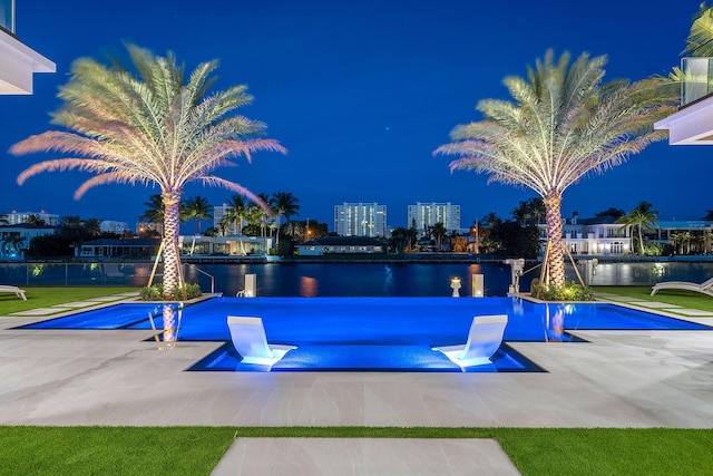 pool at night featuring a patio area and a water view