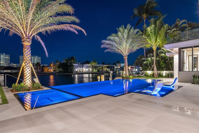 pool at twilight featuring a water view and a patio area