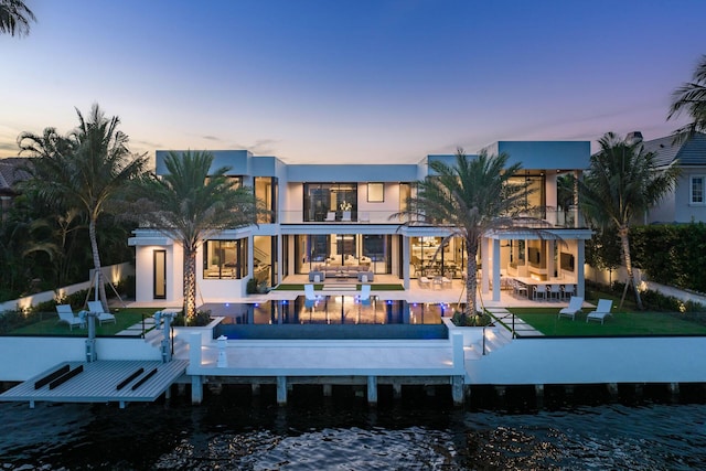 back house at dusk with a yard, a patio, a balcony, and a water view