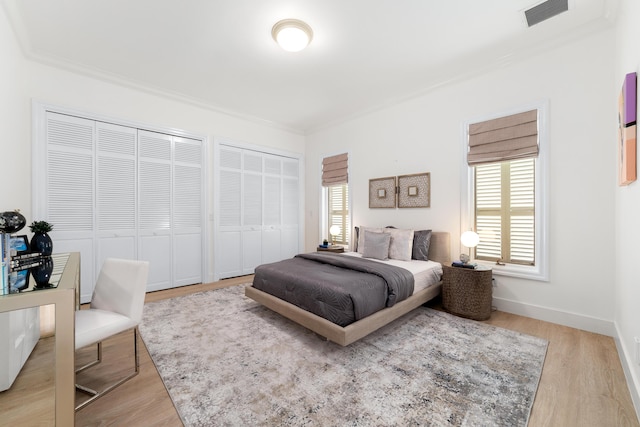 bedroom with crown molding, two closets, and light wood-type flooring