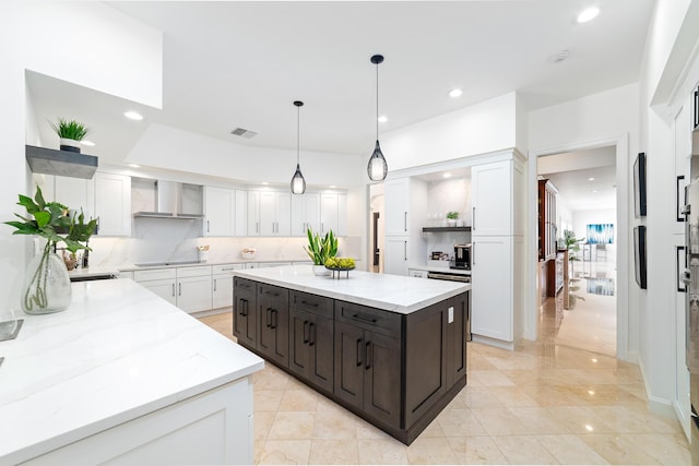 kitchen with wall chimney exhaust hood, hanging light fixtures, a kitchen island, and white cabinets