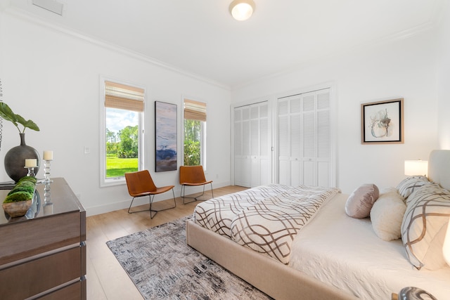 bedroom featuring crown molding, light wood-type flooring, and two closets