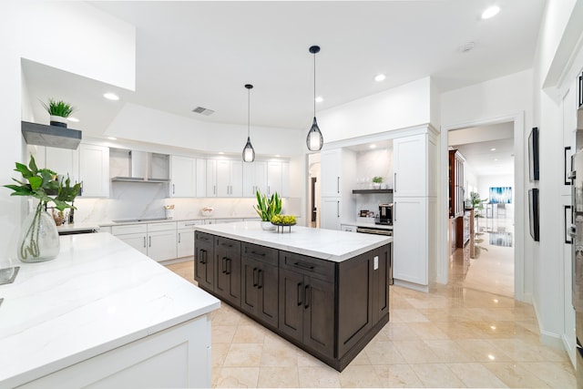 kitchen with white cabinetry, tasteful backsplash, wall chimney range hood, a kitchen island, and decorative light fixtures