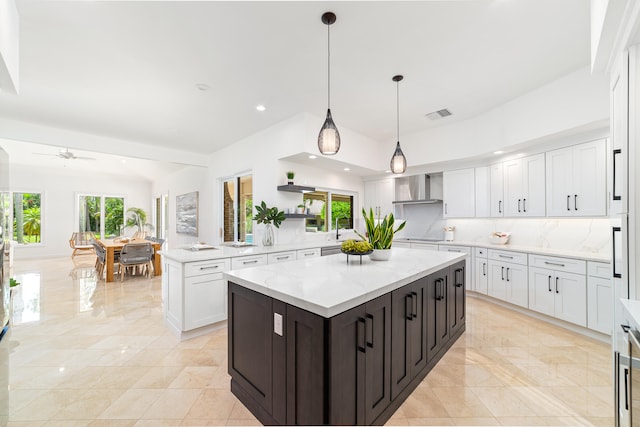 kitchen with light tile patterned flooring, tasteful backsplash, a kitchen island, wall chimney exhaust hood, and pendant lighting