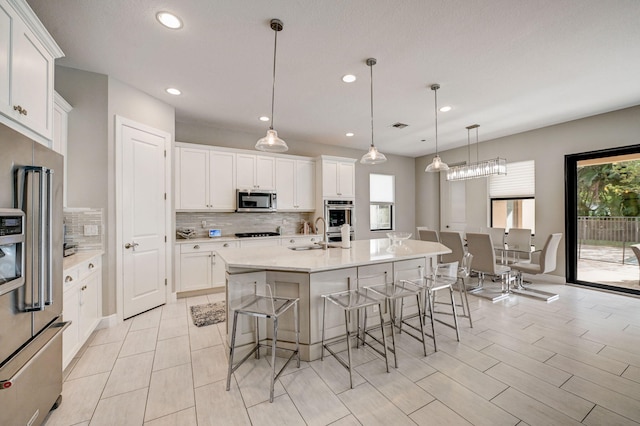 kitchen with decorative light fixtures, an island with sink, stainless steel appliances, and a wealth of natural light