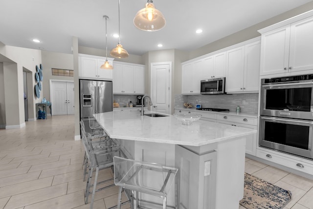 kitchen with hanging light fixtures, an island with sink, white cabinets, stainless steel appliances, and sink