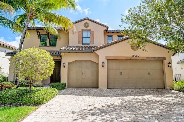 mediterranean / spanish-style house featuring decorative driveway, a tiled roof, an attached garage, and stucco siding