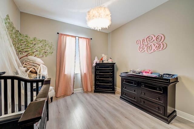 bedroom with a nursery area, light hardwood / wood-style flooring, and a chandelier