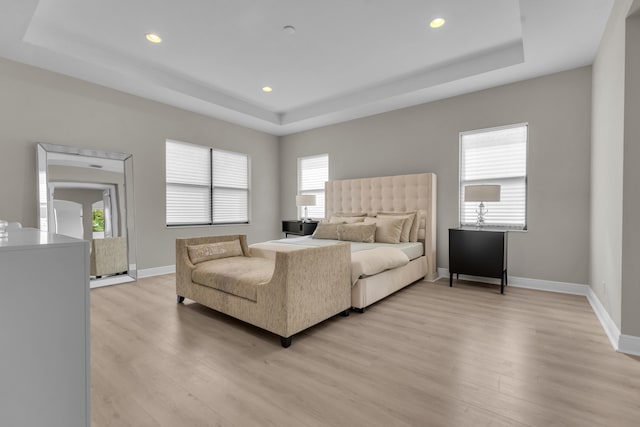 bedroom with light wood-type flooring, a tray ceiling, and multiple windows